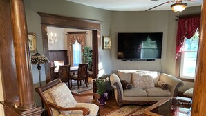 A living room with a sofa, armchair, and coffee table, a dining area with a table and chairs, and a television mounted on the wall.