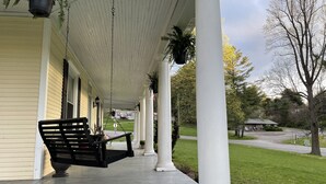 A covered porch with a bench, white columns, and hanging plants.