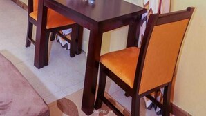 Ruokailutilassa on puinen pöytä ja neljä tuolia, joista kahdessa on oranssit istuintyynyt.