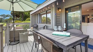 Eine Terrass mit Holztisch, Korbstühlen und einem grünen Sonnenschirm.
