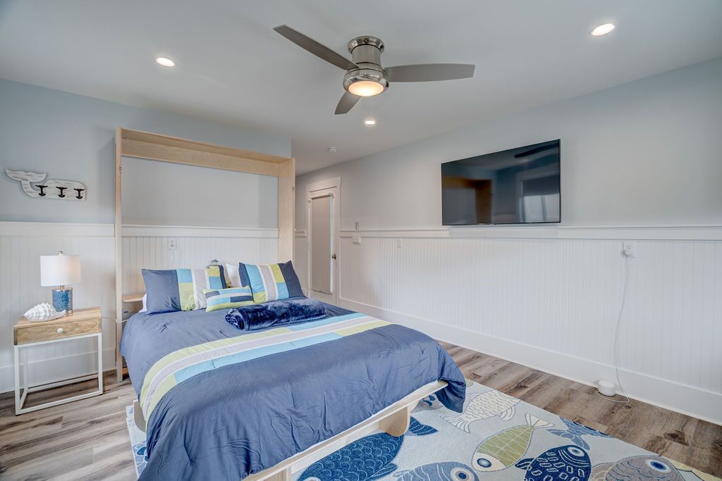 A bedroom with a bed, a nightstand, a ceiling fan, a TV, and a door.