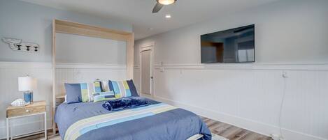 A bedroom with a bed, a nightstand, a ceiling fan, a TV, and a door.