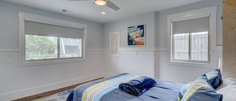 Un dormitorio con una cama, un ventilador de techo y dos ventanas con persianas.
