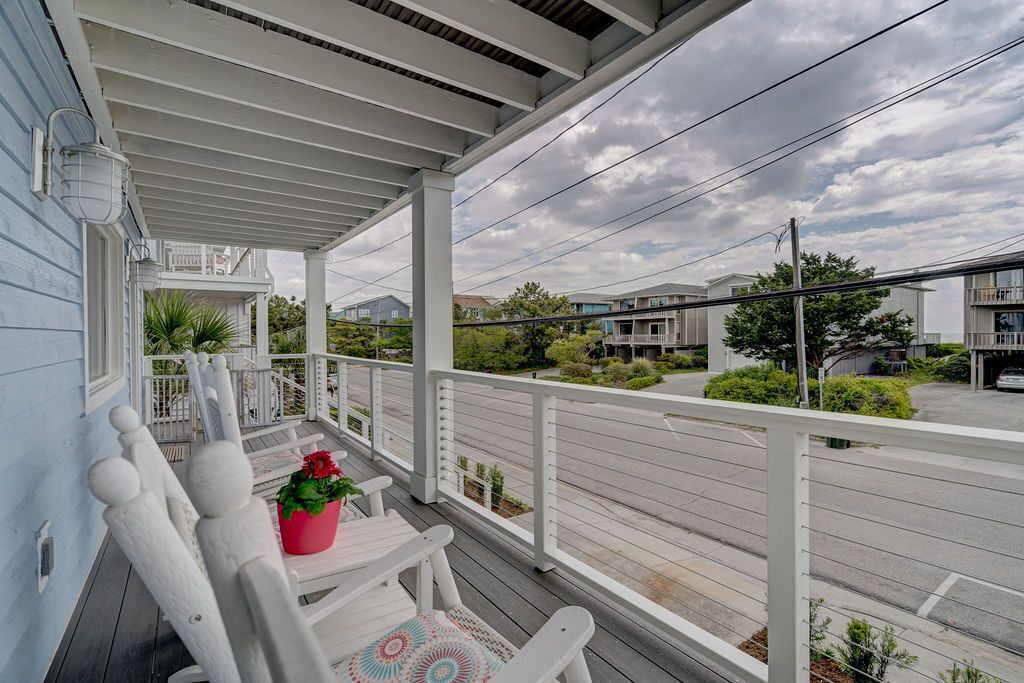 A covered porch with white railings, a seating area with a red flower pot, and a view of a street with houses and a car.