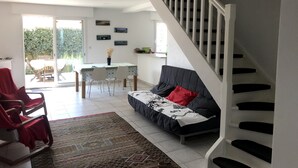 A living room with a sofa, a red chair, a dining table with chairs, and a staircase.