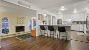 Une cuisine moderne avec des meubles blancs, un îlot central doté de tabourets, un four encastré et un four à micro-ondes.