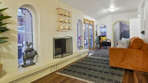 Un salon avec une cheminée, un canapé et une table basse. Il y a deux fenêtres à arc et un miroir au-dessus de la cheminée.