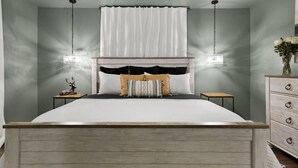 Une chambre à coucher avec un lit en bois, une literie blanche, une tête de lit agrémentée de rideaux, des tables de chevet et une commode.