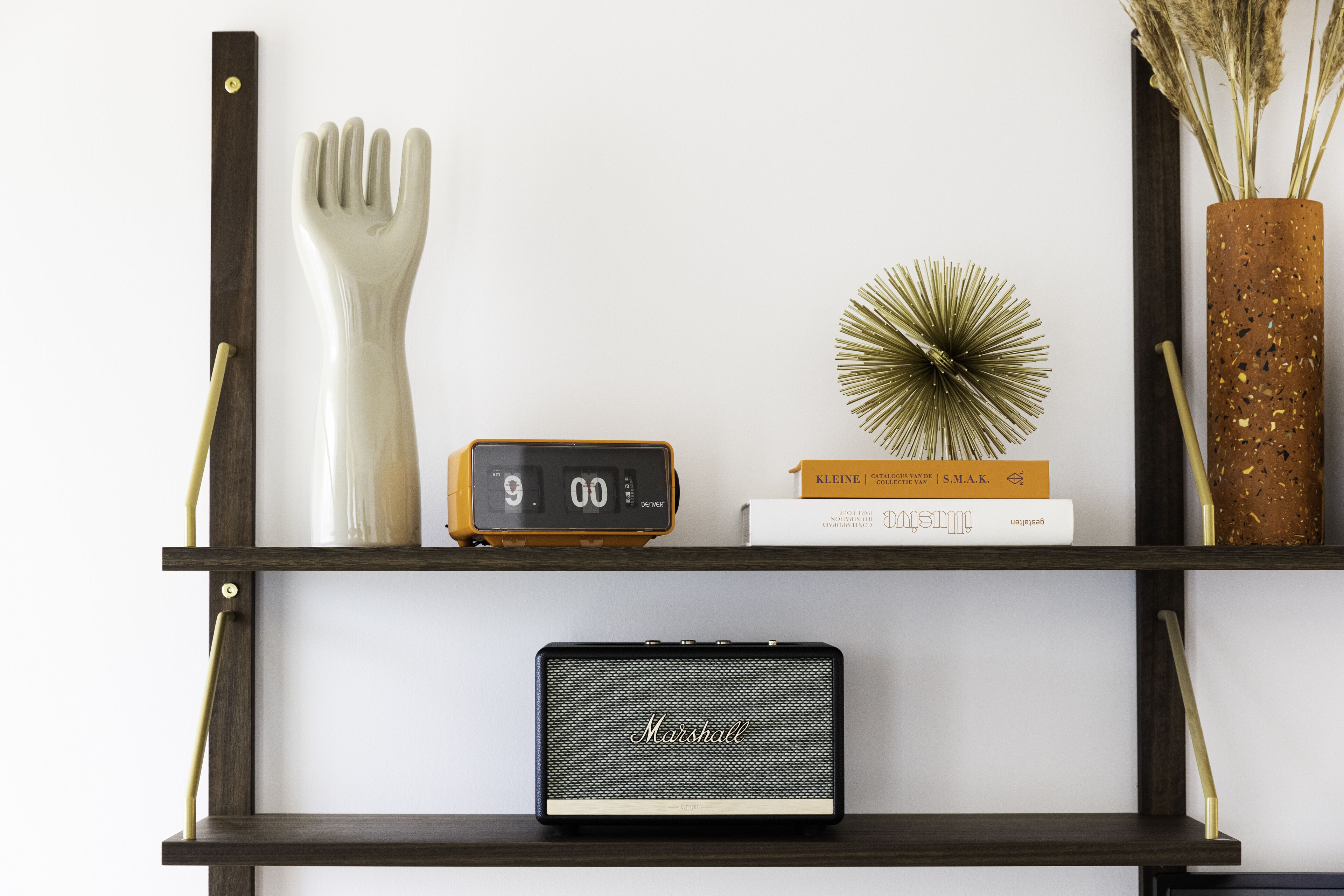 Une étagère avec une cuillère en céramique blanche, une horloge numérique, un petit haut-parleur, une plante décorative et un livre.