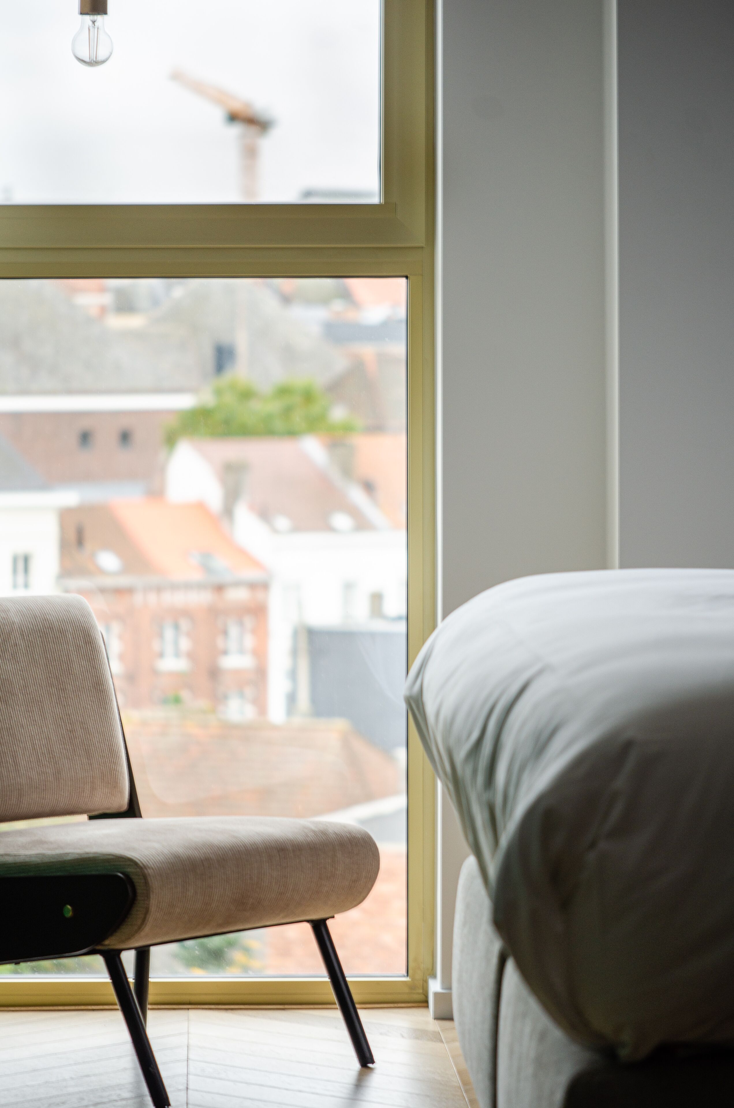 Un dormitorio con cama, una silla y ventana con vistas a la ciudad.