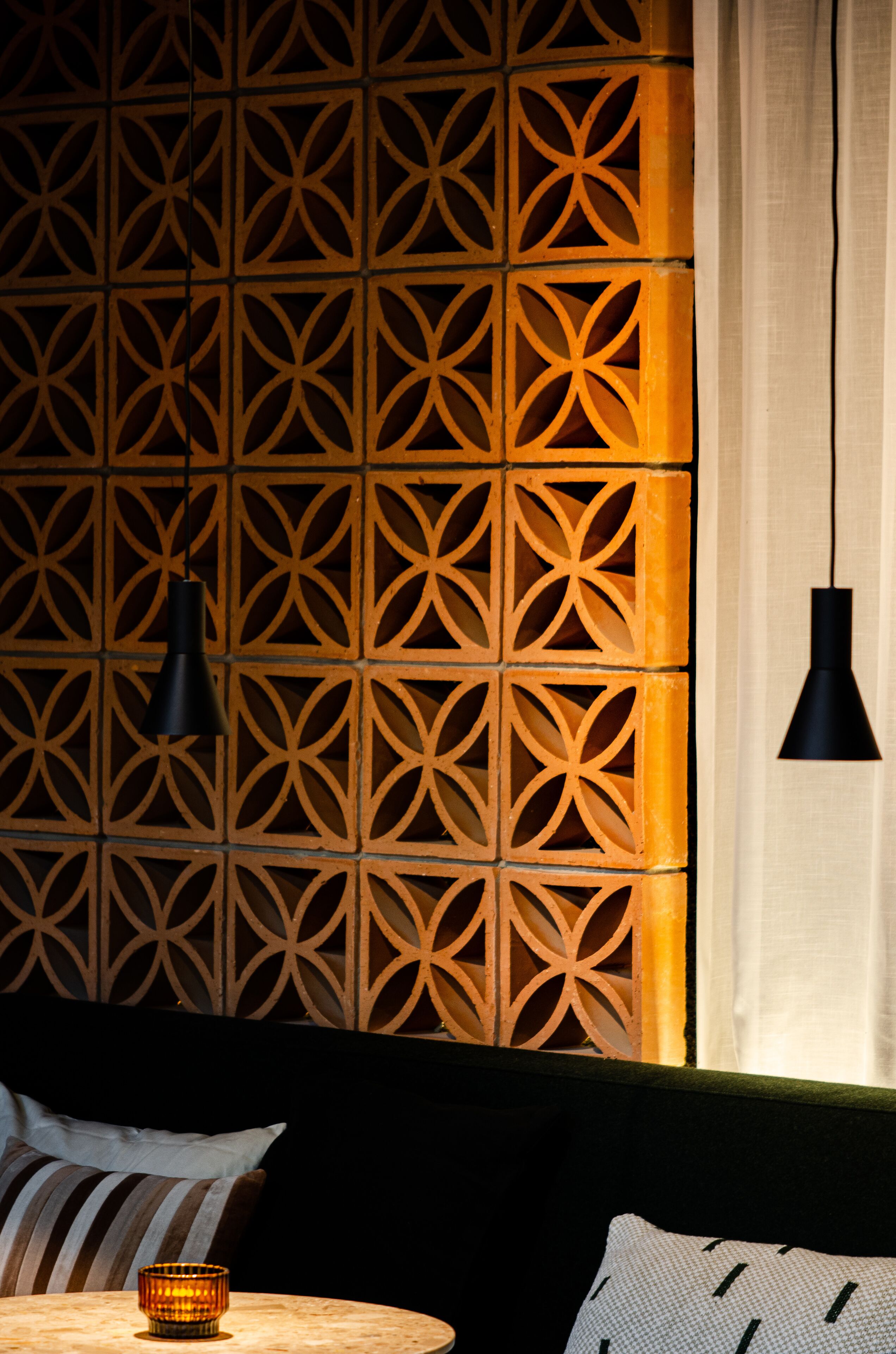 A room with a geometric patterned wall, a round table with a candle, and two black pendant lights.