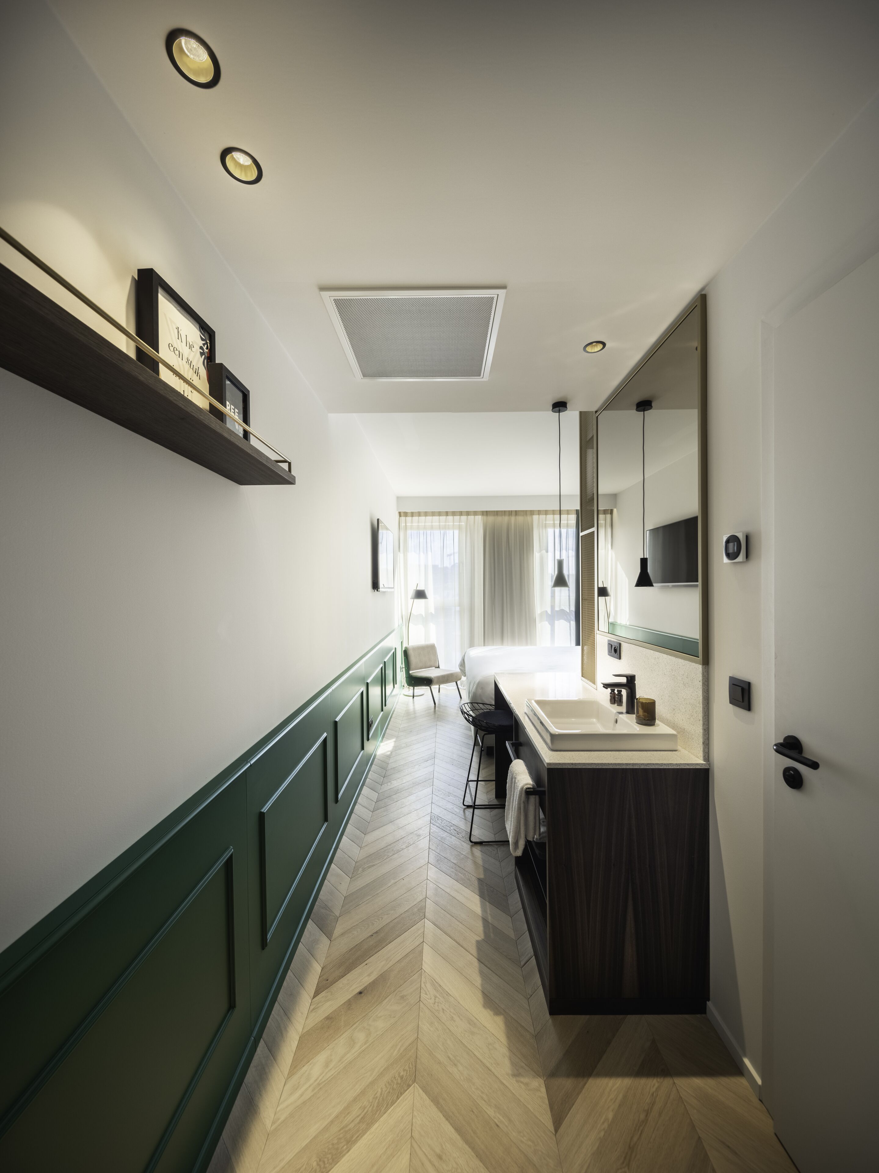 A modern hotel bathroom with a large mirror, a sink, and a chair.