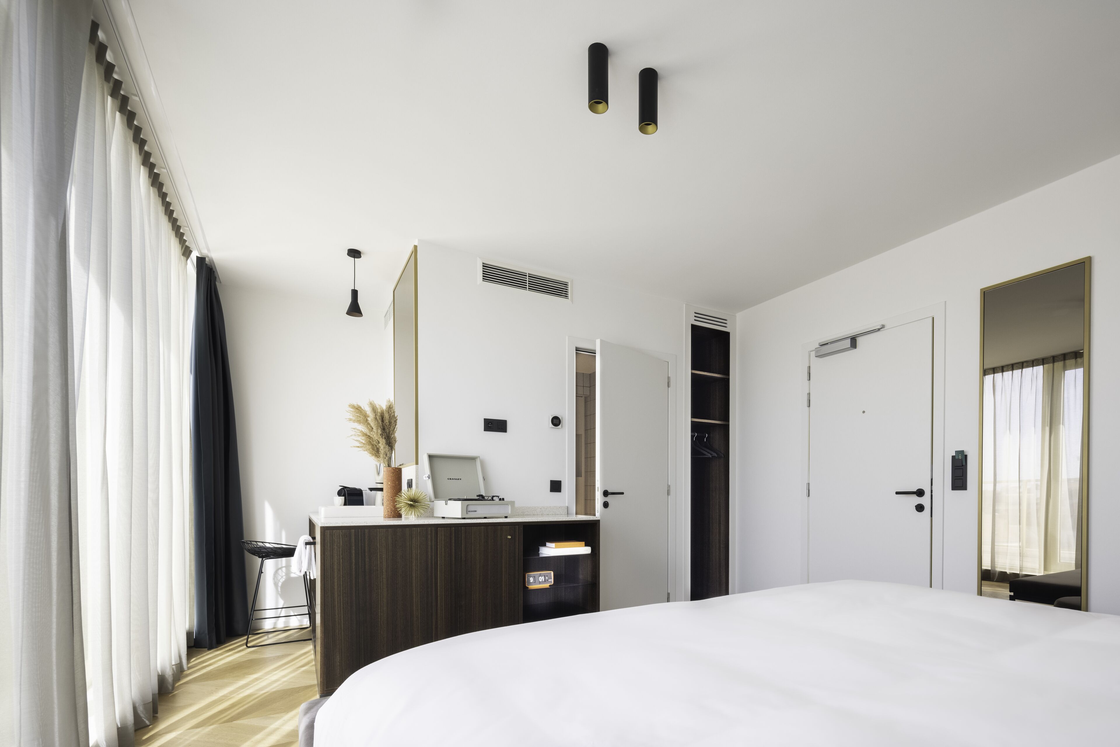 Quarto de hotel com uma cama grande, uma escrivaninha com computador, um guarda-roupa e um espelho.
