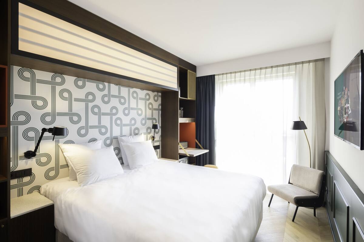 Et moderne hotelværelse med en stor seng, et skrivebord, en stol og et fjernsyn på væggen.
