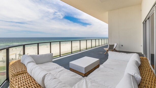 A balcony with a view of the beach, a white sofa, and a small table.