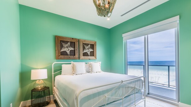 A bedroom with a bed, a nightstand, a lamp, and a view of the ocean. - Wrap Around BF Balcony ~ 6 BR Gulf Front Condo (Gulf Shores)