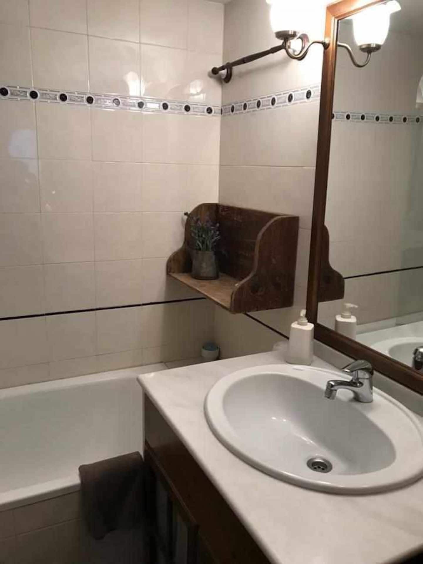 Un bagno con un lavandino bianco, uno specchio e una mensola in legno con articoli da toilette.