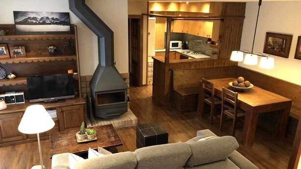 A modern living room with a fireplace, wooden furniture, and a dining area with a kitchen in the background. - Bellver Center (Bellver de Cerdaña)