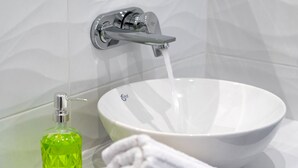 A bathroom with a white sink, a faucet, and a green bottle of soap. - GK in Santorini Home ART (Santorini)