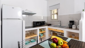 A modern kitchen with white cabinets, a microwave, a coffee maker, and a fruit bowl on the counter. - GK in Santorini Home ART (Santorini)