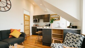 Una cocina moderna con una isla central, un comedor con una silla estampada y una sala de estar con sofá y mesa de centro.