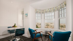 Una habitación moderna con una mesa redonda, dos sillas azules y vistas a la ciudad a través de amplios ventanales.