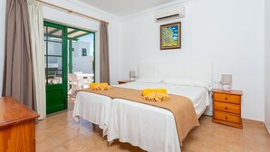 Une chambre d’hôtel avec deux lits, une commode en bois, un bureau et une porte verte donnant sur l’extérieur.