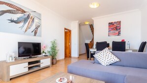 Un salon moderne avec un téléviseur à écran plat, un canapé, une table basse et un coin repas à l’arrière-plan.