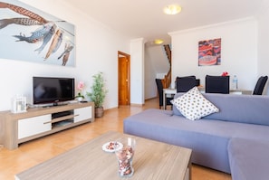 Un salon moderne avec un téléviseur à écran plat, un canapé, une table basse et un coin repas à l’arrière-plan.