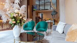 Een modern interieur met een glazen salontafel, teal fauteuils, een grijze bank en een witte vaas met bloemen.