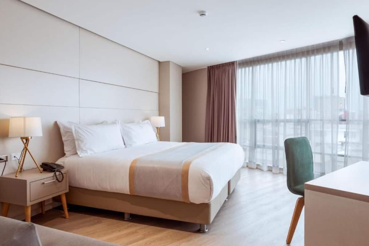 A hotel room with a bed, bedside tables, a desk, and a chair.