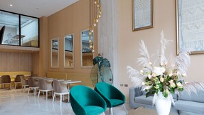 Een moderne hotellobby met turquoise stoelen, een witte vaas met bloemen en een grijze bank.