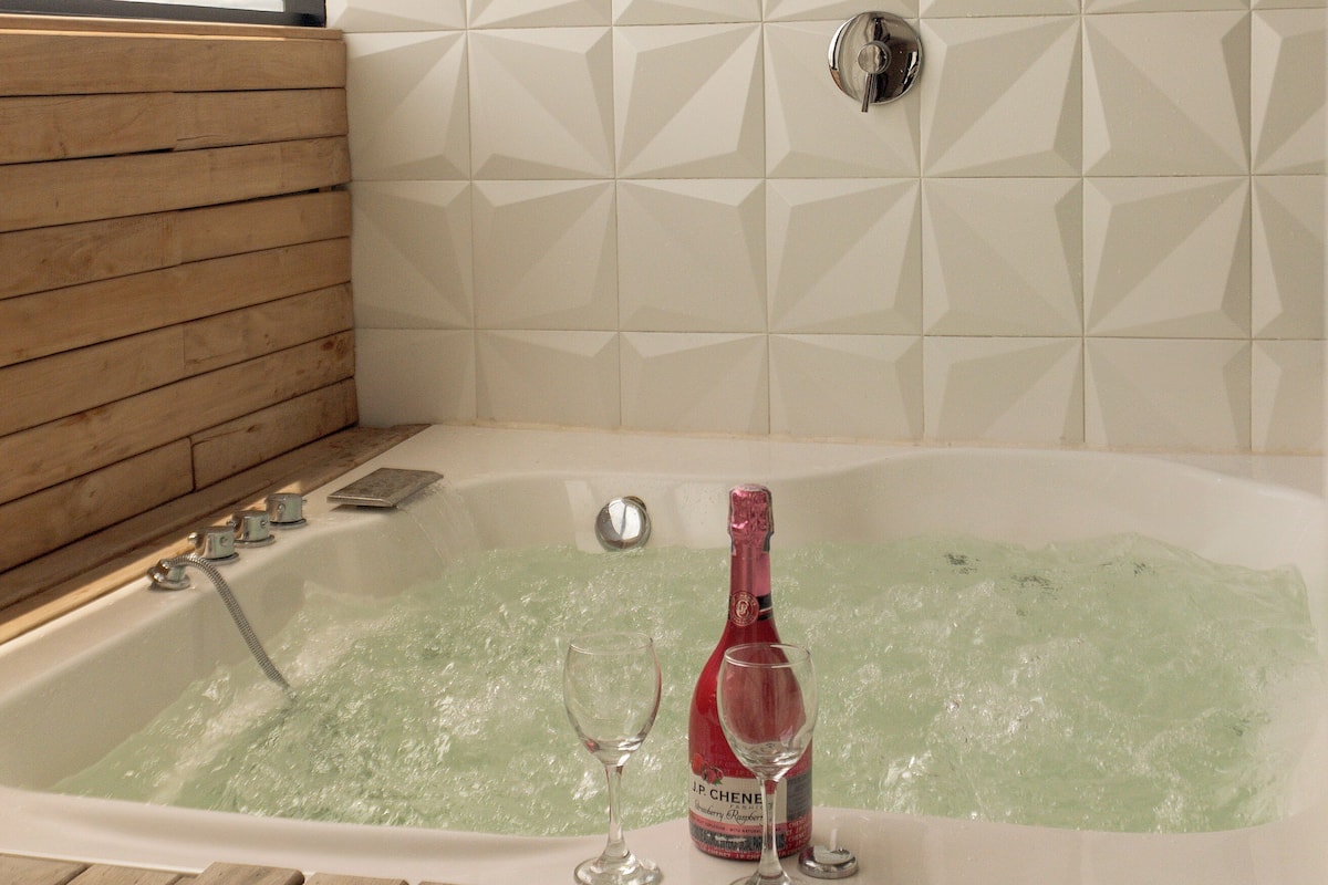 A bathtub with a champagne bottle and glass, wooden paneling, and a geometric tile wall.