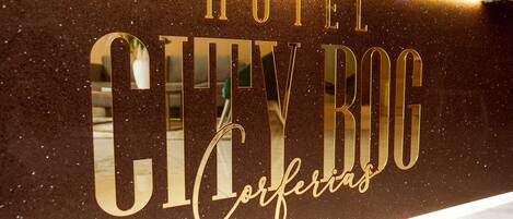 Een bord met de tekst 'HOTEL CITY BOG Corferias' in gouden letters op een structuurwand.