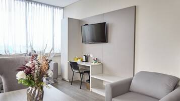 Una sala de estar moderna con un televisor de pantalla plana en la pared, un sofá gris, una mesa de comedor con un jarrón de flores y un sillón gris.