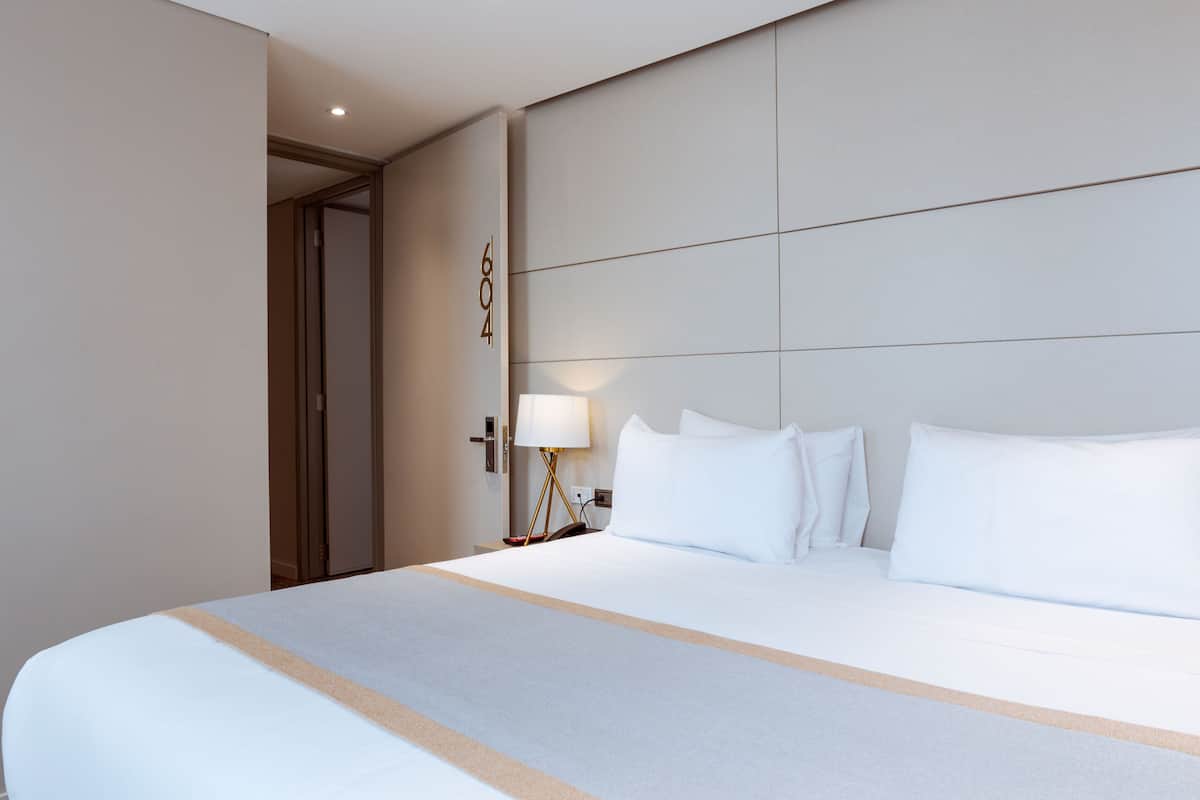 A hotel room with a large bed, a nightstand with a lamp, and a door with a number.
