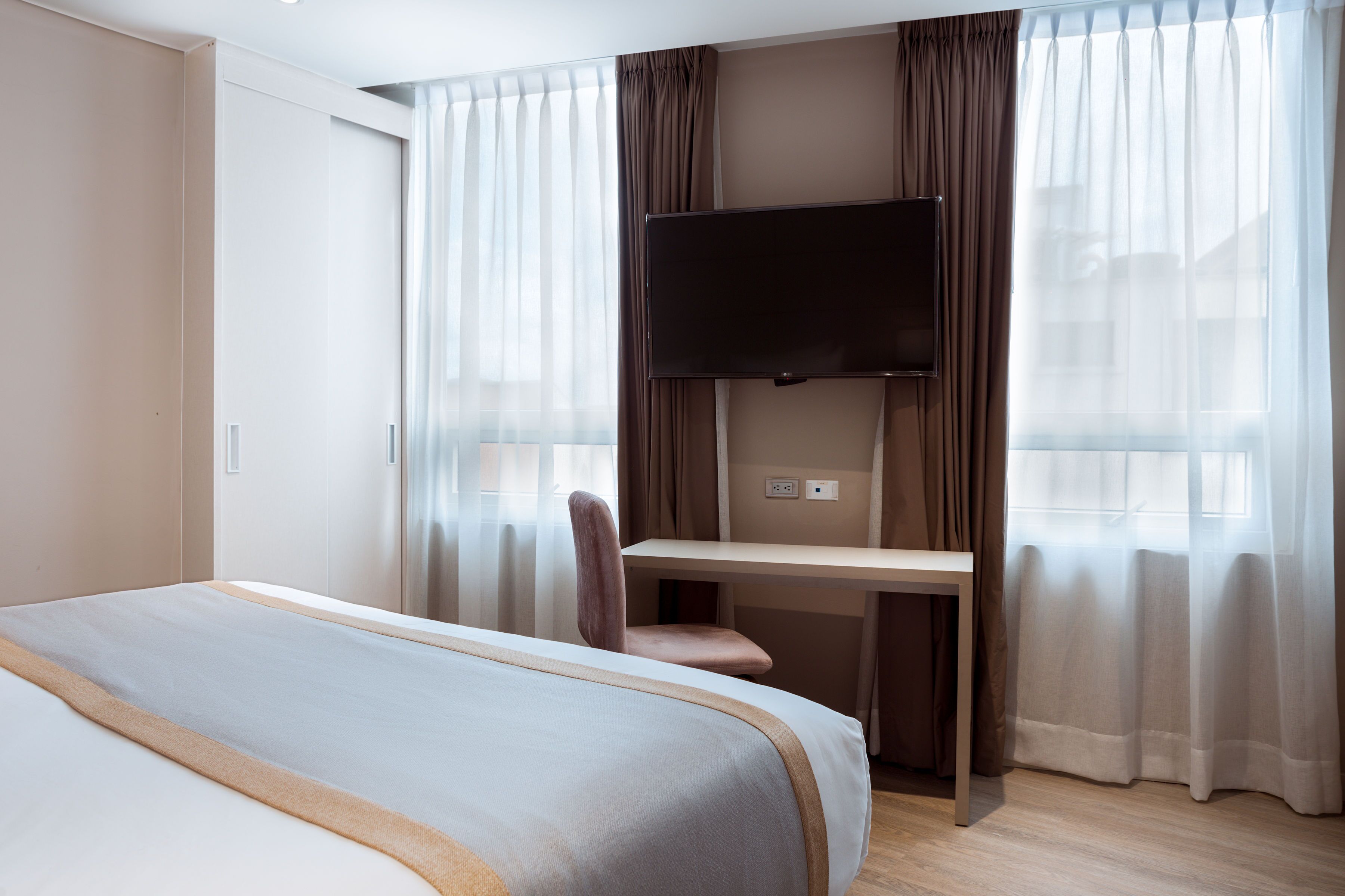A hotel room with a bed, a desk, a chair, a television, and curtains.
