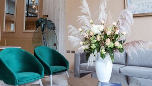 Een moderne woonkamer met blauwgroene fauteuils, een ronde salontafel en een grote vaas met bloemen.