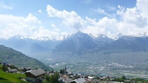 A mountainous landscape with snow-capped peaks, a valley with scattered buildings, and a clear sky.