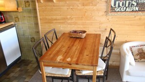 Een houten eettafel met vier stoelen, een fruitmand en een witte bank met een knuffelkussen.