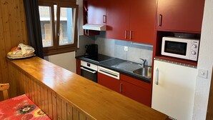 Cocina compacta con armarios de madera, microondas, lavamanos y ventana con cortinas.