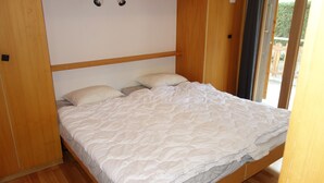 Una cama individual con colcha blanca en una habitación con suelo de madera y cabecero de madera.