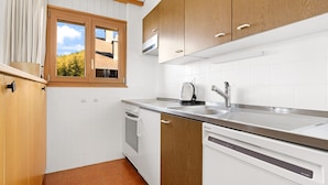Eine moderne Küche mit weißen Schränken, einem Einbauofen, einem Geschirrspüler und einem Fenster mit Blick auf Bäume.