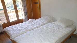 A double bed with a quilted white duvet, wooden headboard, and a view of a wooden deck through a sliding glass door.