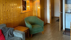 Una sala de estar acogedora con una pared de madera, un sillón verde, un sofá gris y una mesa de centro de madera.