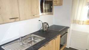 Een keuken met houten kastjes, een roestvrijstalen spoelbak, een waterkoker, een magnetron en een oven.