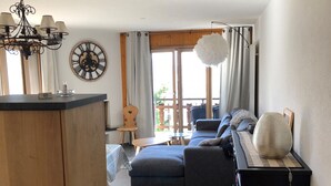 Een moderne woonkamer met een bank, een houten kast, een eethoek met een tafel en uitzicht door een groot raam.