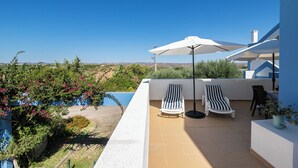 Eine Dachterrasse mit zwei Liegestühlen, einem großen Sonnenschirm und Blick auf einen Pool und die Landschaft.