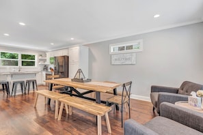 A modern kitchen with white cabinets, a stainless steel refrigerator, and a wooden dining table with benches. - Summer Fun in Helen, GA with Grilling, Hot Tub + Games! (Helen)