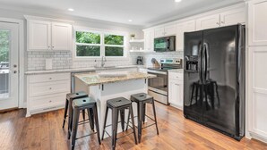 A modern kitchen with white cabinetry, a black refrigerator, and a central island with stools. - Helen, Georgia ★ Yonah Mtn, Hot Tub, Games + Grill (Helen)